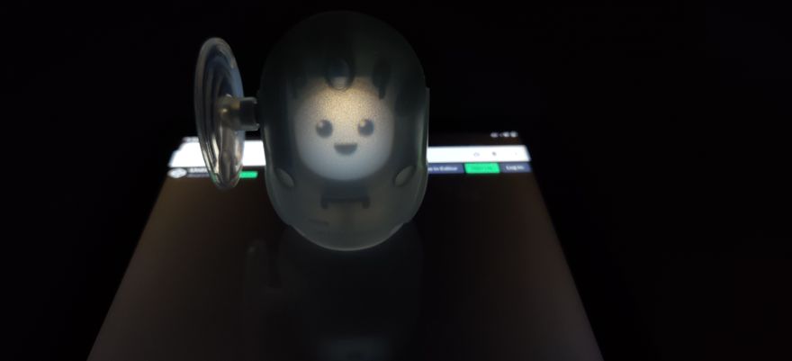 Photography of the toy in a dark room. It is placed on top of a tablet, and a smiling face is illuminating it