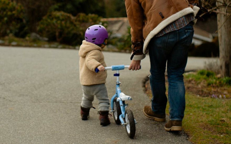 A little kid pushes a bicycle with the help of an adult