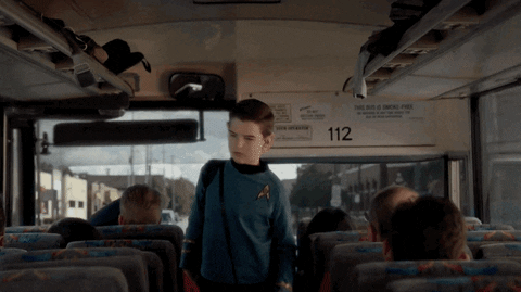 Child walking onto a bus dressed as Spock and waving at a bunch of others with the Vulcan salute.