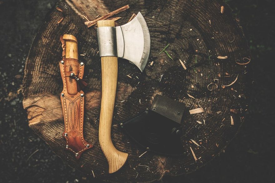 A bushcraft knife and an axe laying on a tree stump